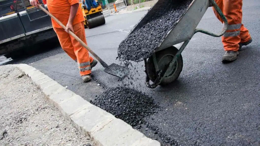 Two men are working on a road with a wheelbarrow.