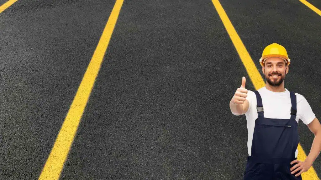 A man in a hard hat is giving a thumbs up in a parking lot.