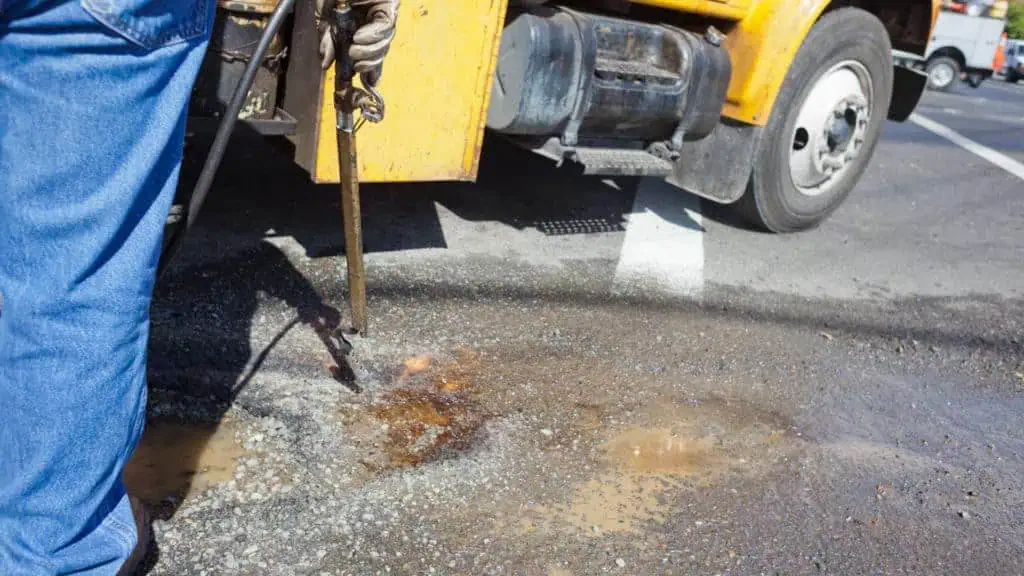 A man repairing a pothole with a hose.