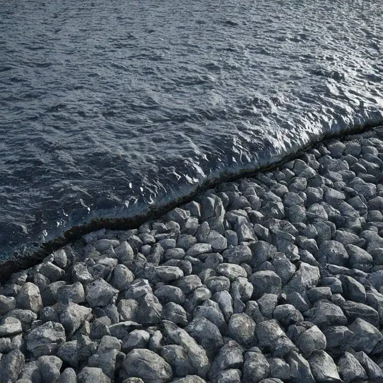 A stone breakwater meets the calm waters of a body of water, with small waves gently lapping against the rocks.