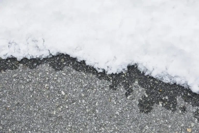 A close-up image shows the edge of a layer of snow on what appears to be asphalt pavement.