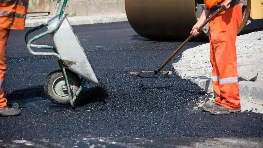 Two men working on a paved road with a wheelbarrow.