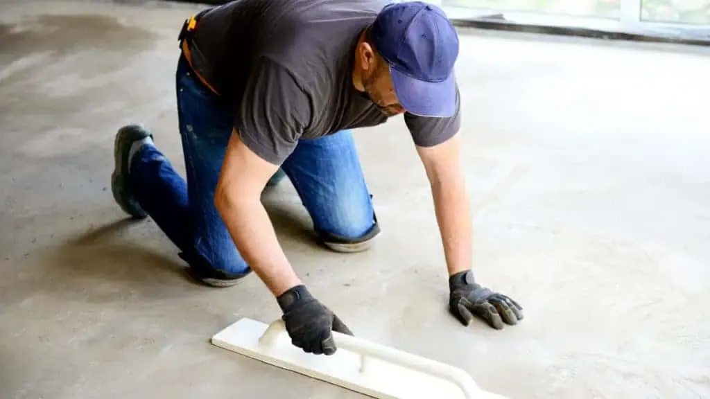 A man is laying concrete on a floor.