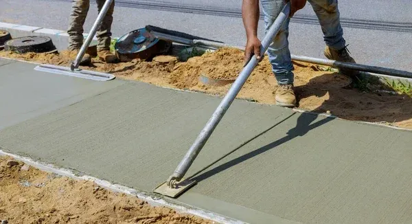 A man is performing sidewalk repair by pouring concrete on a sidewalk.