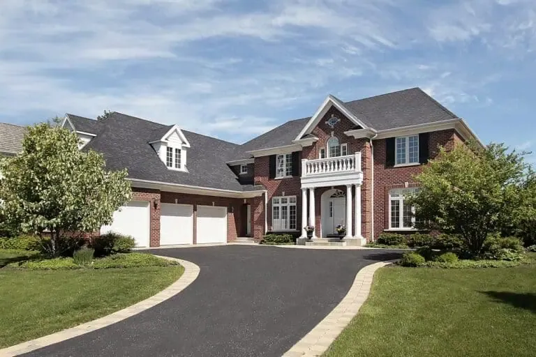 Large brick house with a white-columned entrance and three-car garage, set against a sunny sky with a manicured lawn.