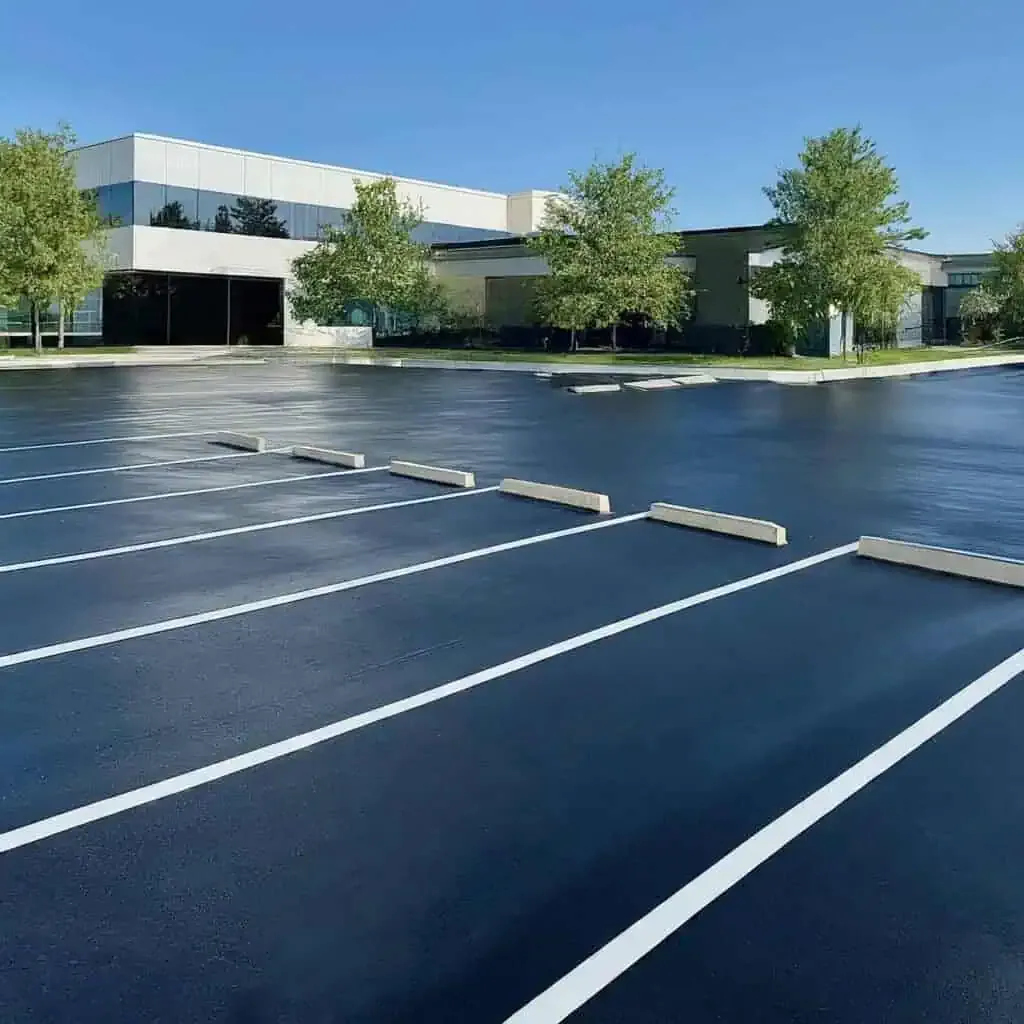 An empty, newly painted parking lot with a modern office building and trees in the background under a clear blue sky.