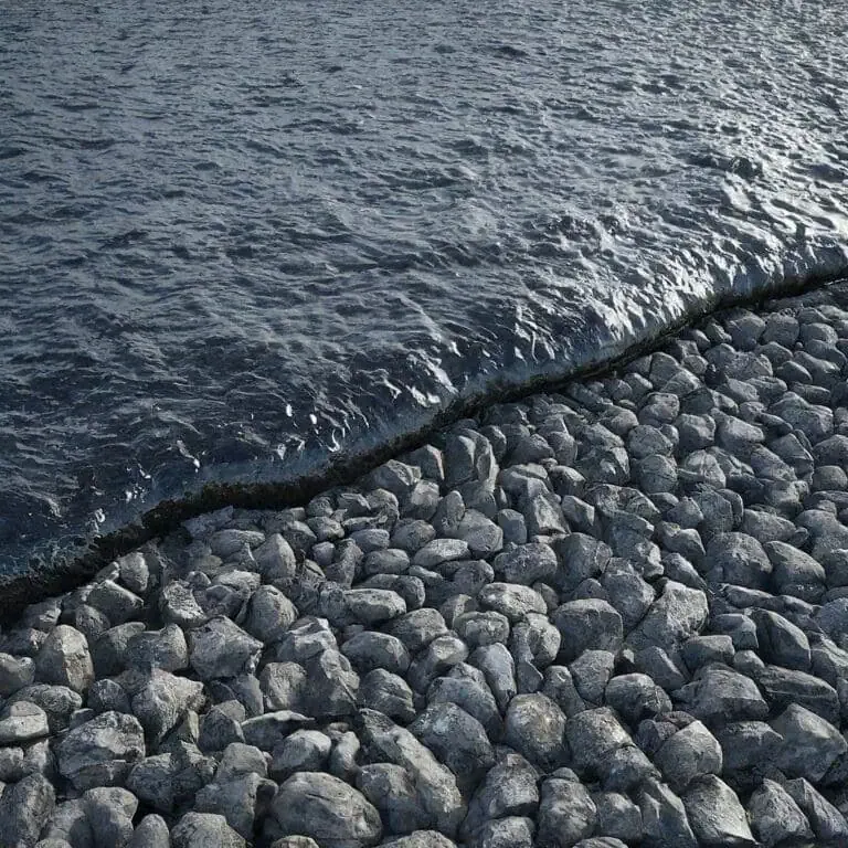 A stone breakwater meets the calm waters of a body of water, with small waves gently lapping against the rocks.