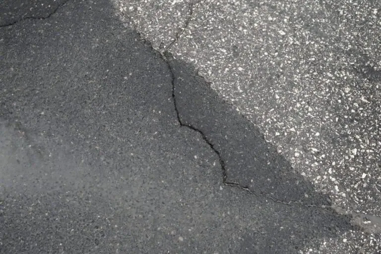 A crack in an asphalt road surface showing a mix of dark and light textures.