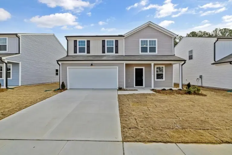 A two-story house with a gray exterior, a two-car garage, and a newly laid lawn, situated between similar homes under a blue sky with clouds.