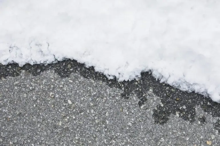 A close-up image shows the edge of a layer of snow on what appears to be asphalt pavement.