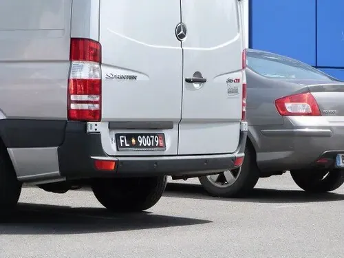 A silver van and a gray sedan are parked side by side in a parking lot on a sunny day.