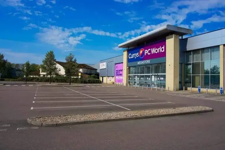 An empty parking lot in front of a large Currys PC World megastore building on a clear day.