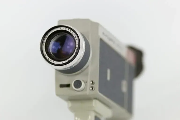 Close-up of a vintage video camera lens with a metallic body. The lens shows the brand 